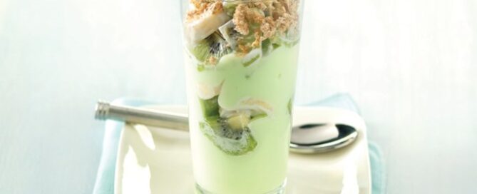 Shredded Wheat Key Lime parfait in a clear glass on a white plate with a silver spoon in the background.