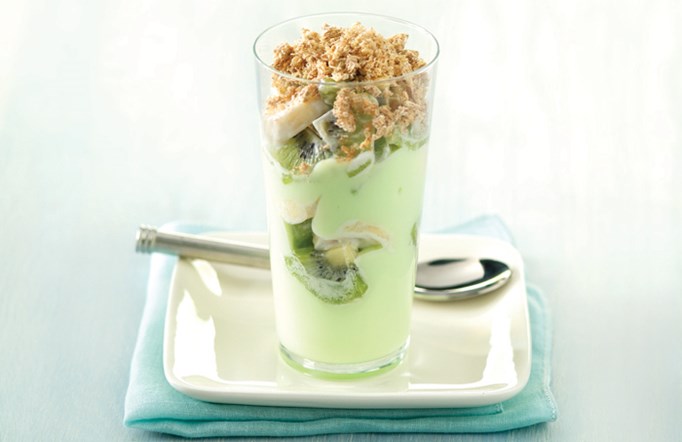 Shredded Wheat Key Lime parfait in a clear glass on a white plate with a silver spoon in the background.