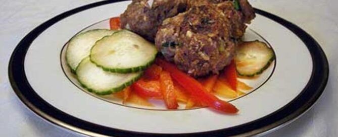 Korean Meatballs on a white plate with a black rim with cucumbers and red peppers on the side.