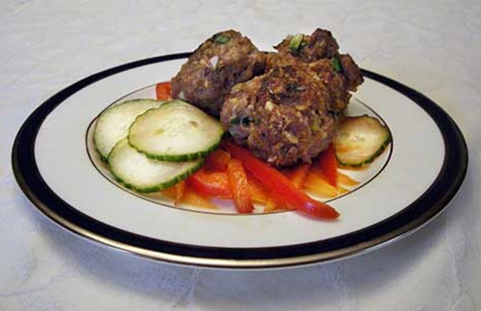 Korean Meatballs on a white plate with a black rim with cucumbers and red peppers on the side.