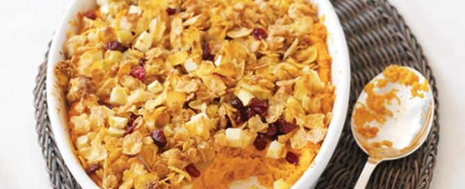 Cranberry Almond Crunch Mom’s Best Sweet Potato Casserole in a white bowl with a spoon on the side.