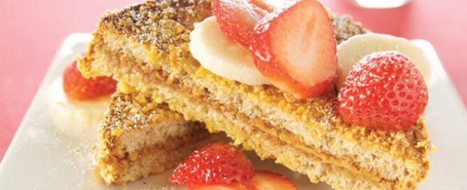 Two pieces of bread on a white plate with strawberries on top.