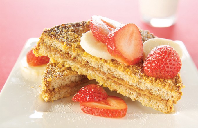 Two pieces of bread on a white plate with strawberries on top.