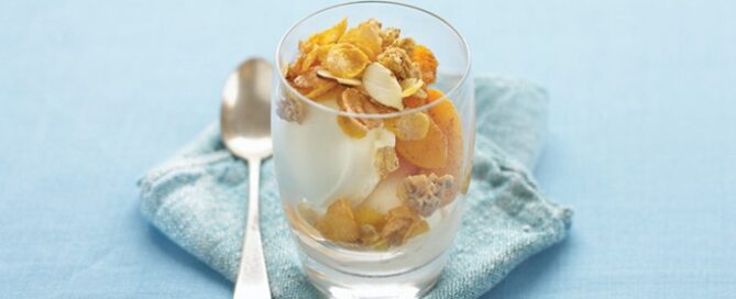 Peach Crisp in a cup on a blue background and napkin with a spoon on the side.