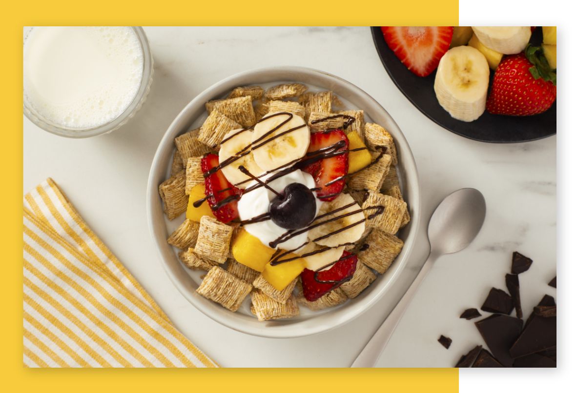 Shredded Wheat in a bowl with strawberries, pineapple and bananas on top with a chocolate drizzle and a cherry.