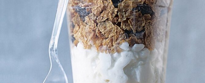 Shredded Wheat a l'orange in a clear cup with a clear spoon on a blue background.