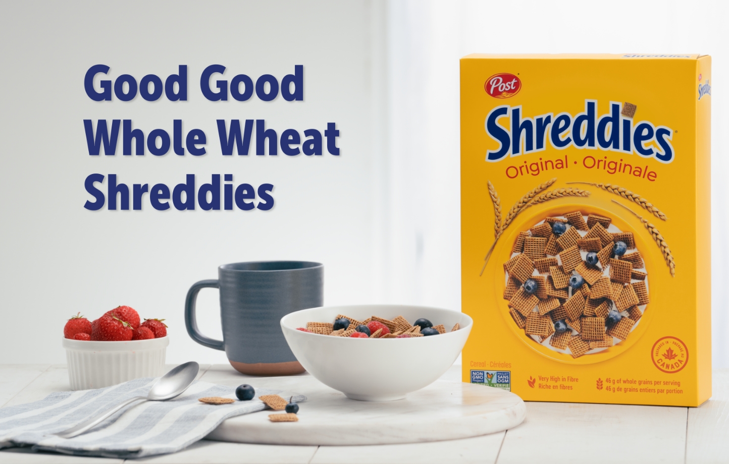 "Good Good Whole Wheat Shreddies" Original Shreddies box sitting on a table with a bowl of cereal with fruit, and a coffee.