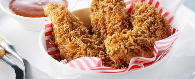 Shreddies Chicken Fingers in a white bowl with dipping sauce on the side.