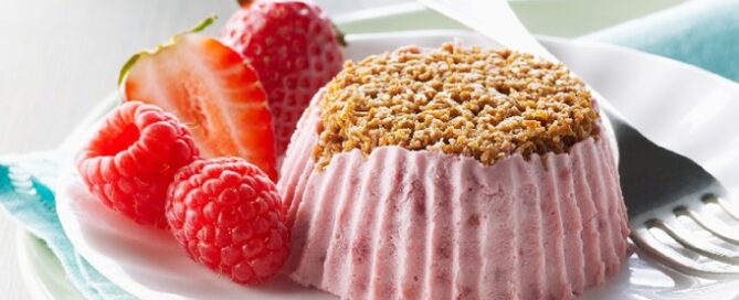 Shreddies Frozen Mini Berry Cheesecake on a white plate with a fork and strawberries on the side.
