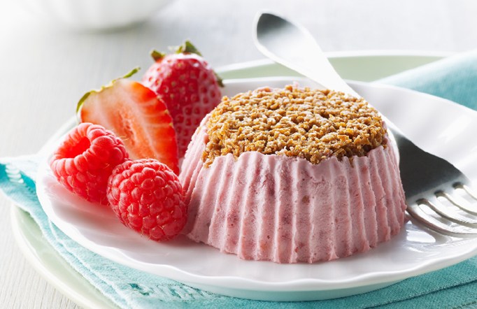 Shreddies Frozen Mini Berry Cheesecake on a white plate with a fork and strawberries on the side.