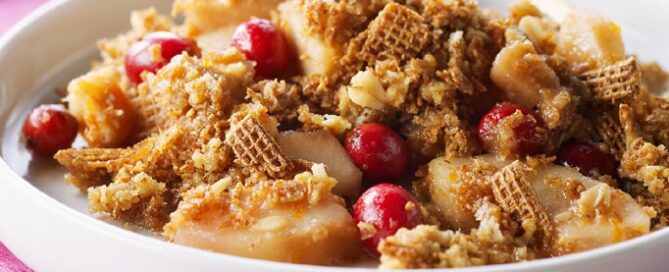 Shreddies Pear Cranberry Crisp in a white bowl on a pink tablecloth.