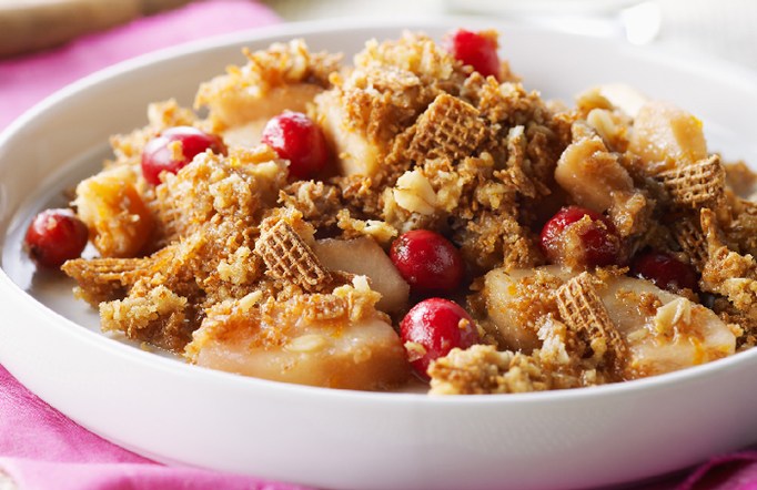 Shreddies Pear Cranberry Crisp in a white bowl on a pink tablecloth.